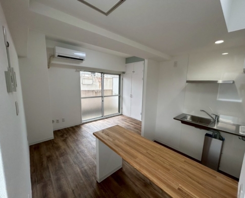 東京都大田区の賃貸マンションで原状回復工事後のキッチンとリビング。新設した木製カウンターと明るいクロスで清潔感ある内装に仕上がった様子