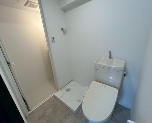 原状回復リフォーム後のトイレと洗濯機置場。東京都大田区の賃貸マンションで、温水洗浄便座付きトイレと新しい防水パンを設置し、明るく清潔感のある空間に仕上げた様子。