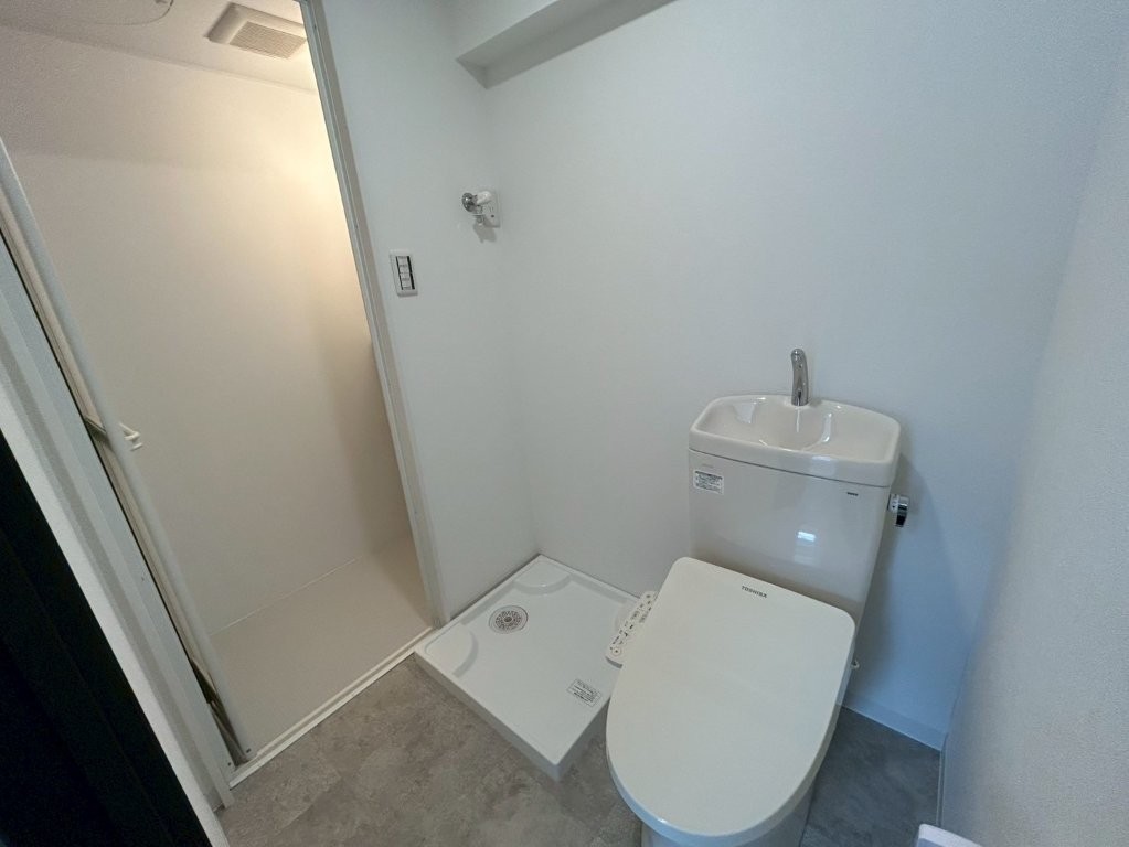 原状回復リフォーム後のトイレと洗濯機置場。東京都大田区の賃貸マンションで、温水洗浄便座付きトイレと新しい防水パンを設置し、明るく清潔感のある空間に仕上げた様子。