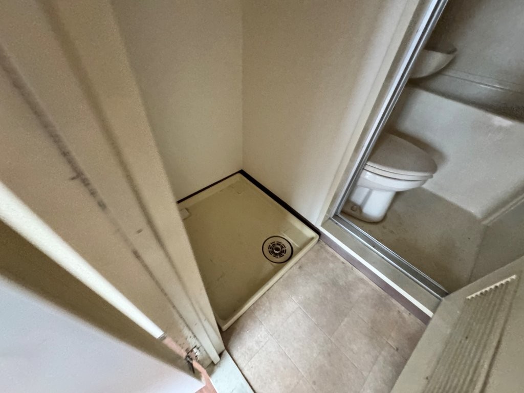 東京都大田区の賃貸マンション原状回復工事前のトイレと洗濯機置場の様子。古いユニット式で、防水パンや床に経年劣化が見られる状態。