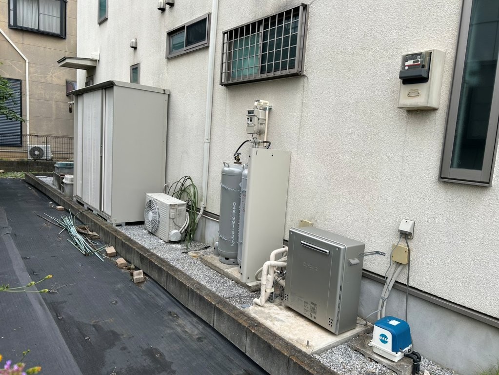 埼玉県久喜市の戸建て住宅で、エコキュートを撤去しLPガス給湯器(24号据置型)を新設した施工後の様子。ガスボンベと給湯器が整然と設置され、安全な配管工事が完了している。